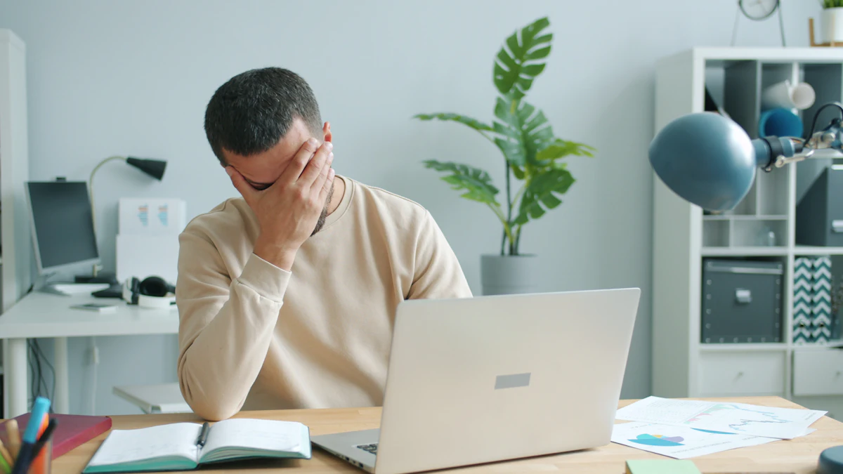 ノートPCの前で額に手を当てて悩む男性